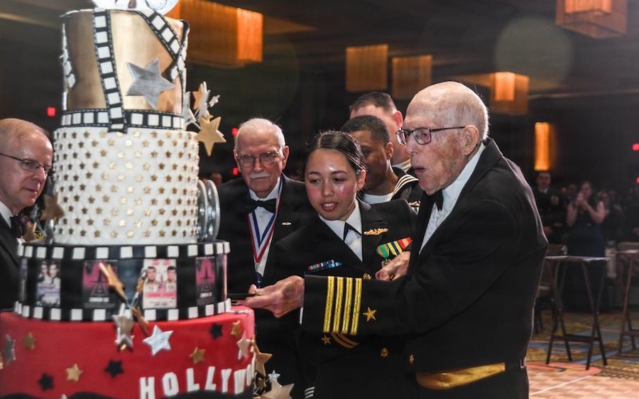young woman and old man in dress uniform cut a large cake
