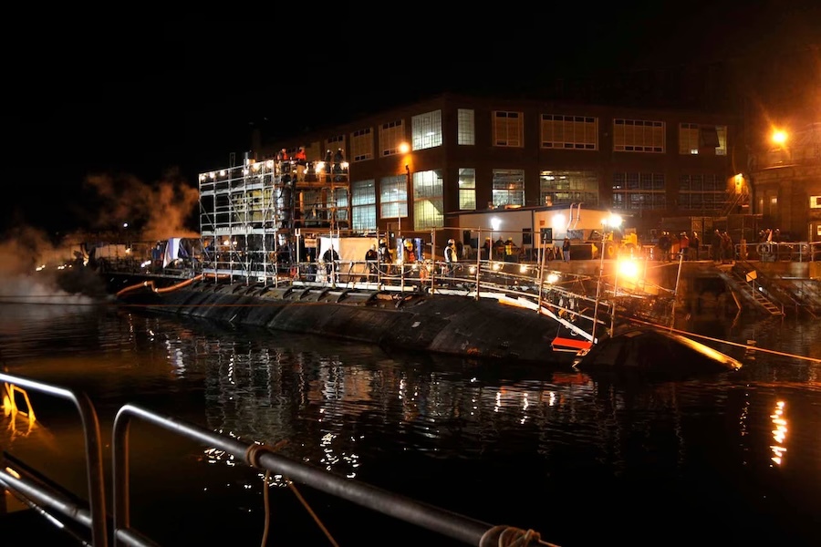surfaced submarine at night in front of a lit-up building