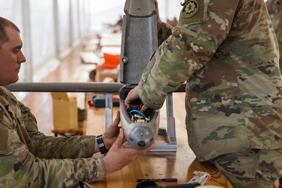 two men in fatiques work with wiring on a drone
