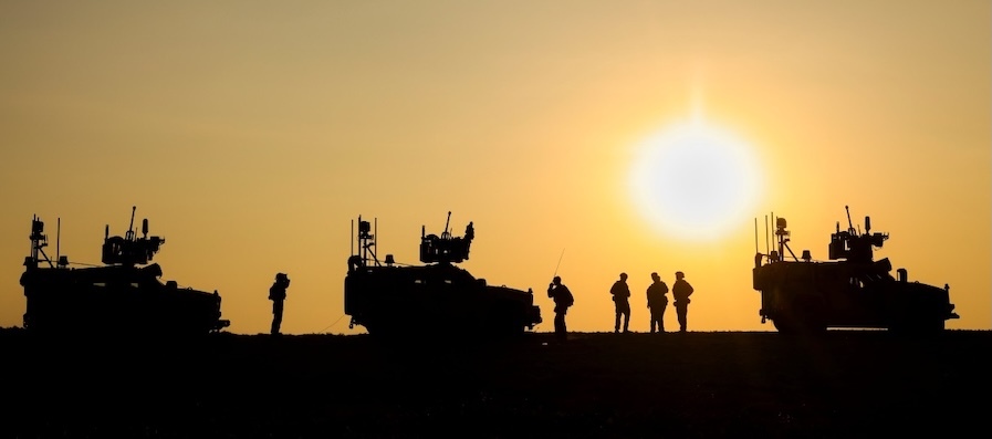 tanks and soldiers silhouetted against a yellow sunset