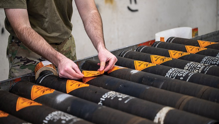 man placing an orange sticker on the barrel of a missile