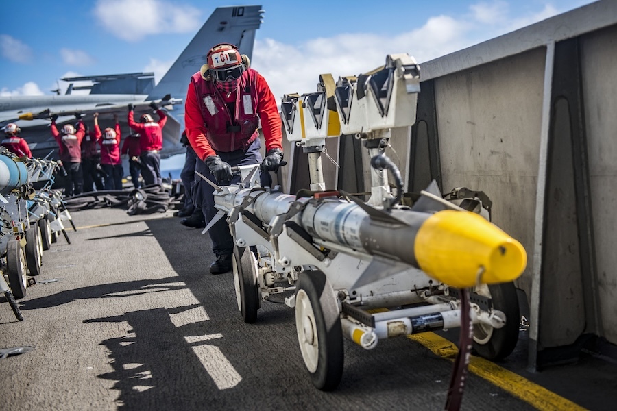 man in a red jacket pushes a missile on a wheeled cart