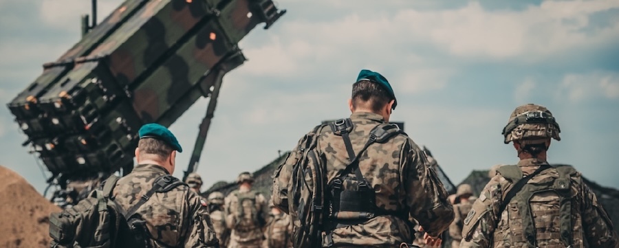 backs to camera, soldiers in fatigues stand near a missile launcher
