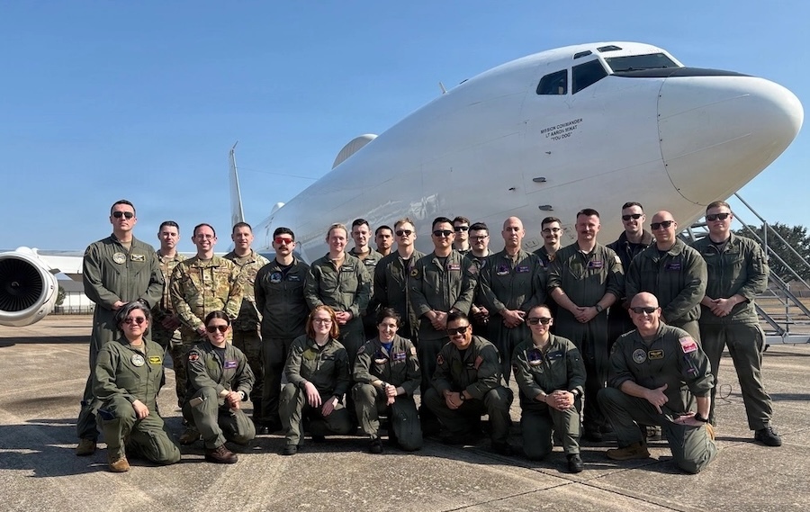 group of airmen pose before the nose of a white E6-B Mercury aircraft