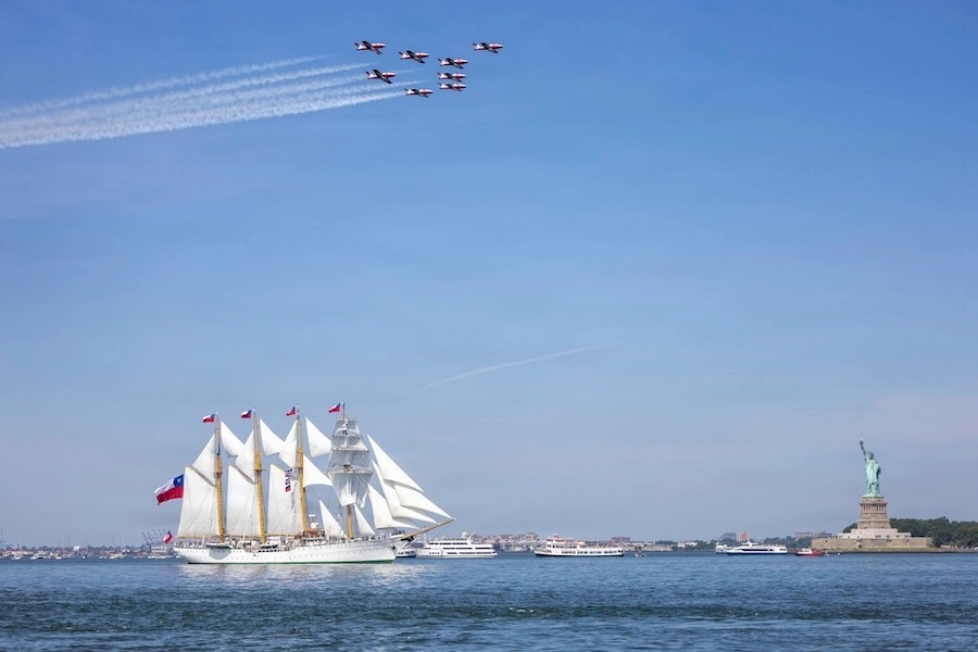 white sailing ship with planes flying overhead and the Statue of Liberty off to the right