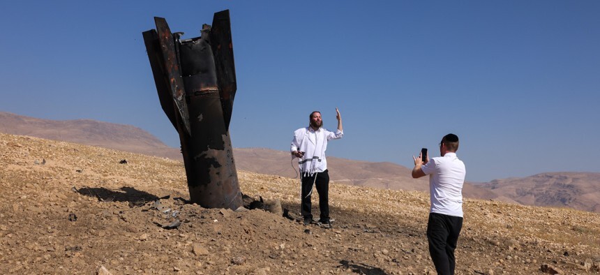 man in white being photographed in front of a half-buried rocket