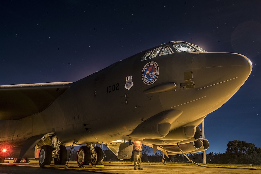 nose of B52 bomber at twilight, with a ground crew member working underneath