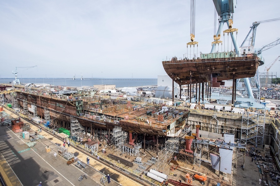 hull of a ship being assembled at a busy shipyard