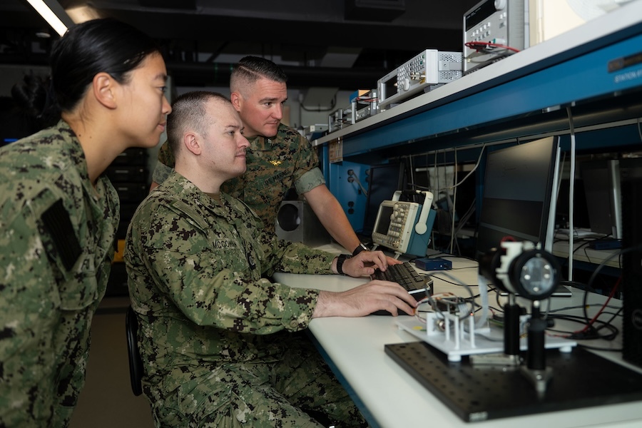 woman and two men in fatiques looking at a computer screen