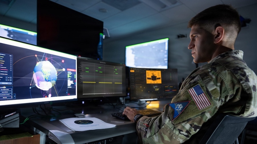man in fatigues seated in front of computer screens