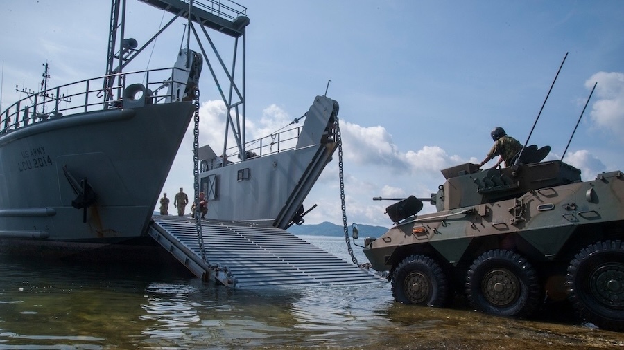 armored vehicle prepares to drive onto a ship's loading ramp