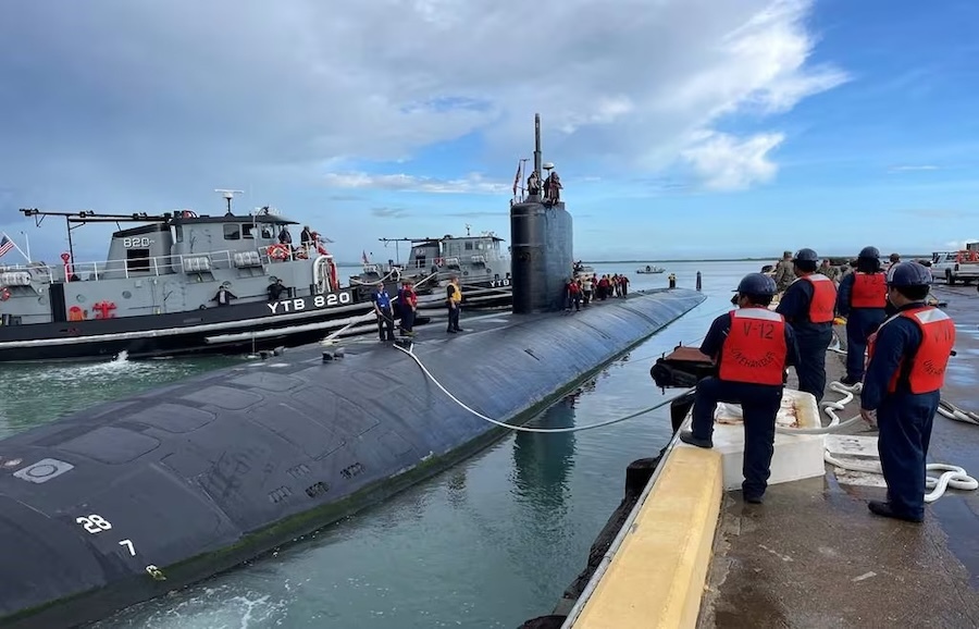 workers stand a pier next to a docked submarine