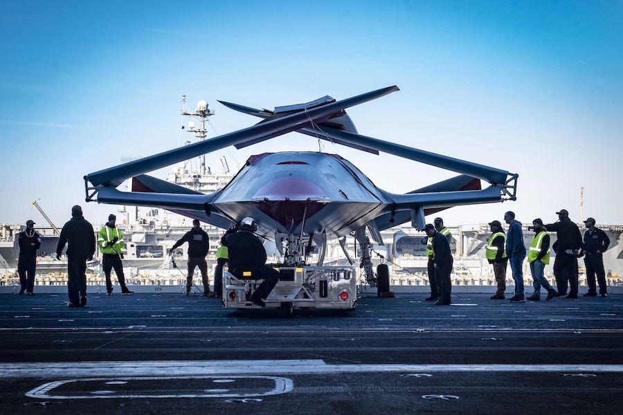 a large drone sits on tarmac with people gathered around