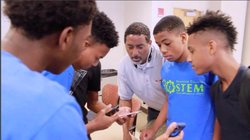 A teacher and a group of students look together at a handheld device