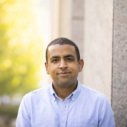 A portrait of a man in front of a blurred exterior background.
