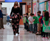 a teacher in a school hallway with a line of masked children