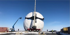 A large white ball being put together with a crane. 