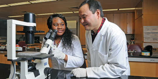 A man and woman in lab coats with a microscope.