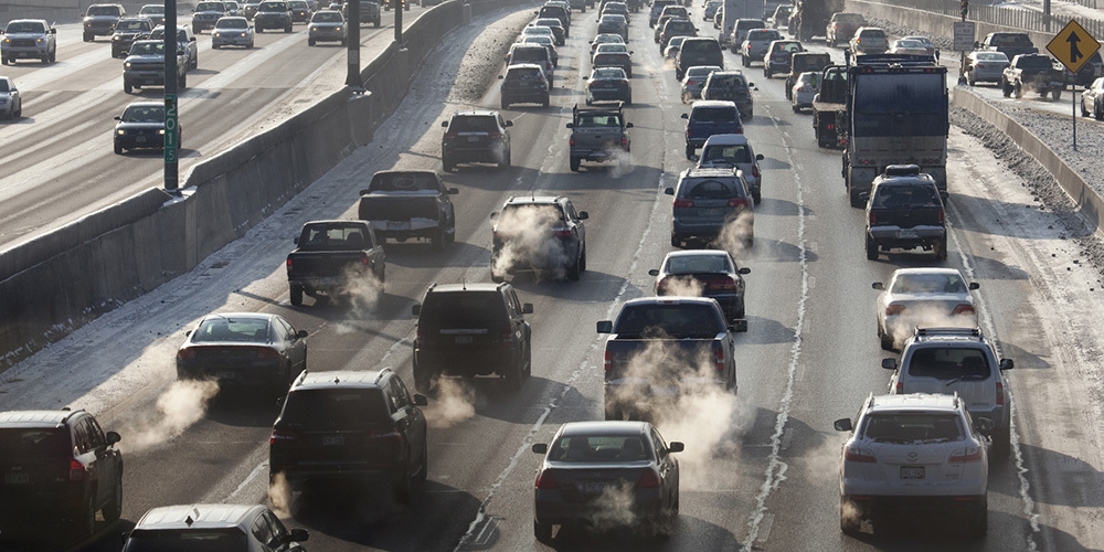 Many cars, trucks and visible exhaust on a busy highway.