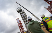 Two researchers watch the last modular component of the 10-story cold-formed steel building being placed by a crane for testing against earthquakes.