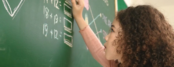 Elementary school student solving math equations at a chalkboard.