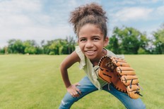 Image shows an African American girl playing baseball