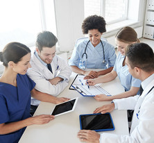 Image shows three female and two male, multi-ethnic health professionals at a table