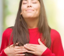 Image shows a Hispanic/Latina woman with her hands placed over her chest/heart.