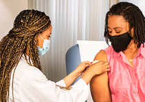 Image shows a Black healthcare professional vaccinating a Black woman