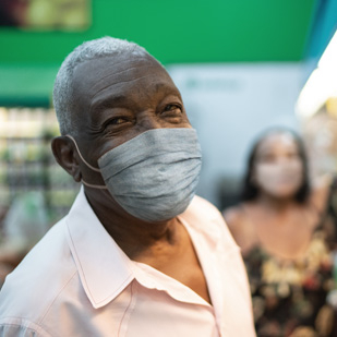 Image shows an older Black/African American man wearing a mask while grocery shopping