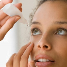 Image shows a young woman of color applying eye drops