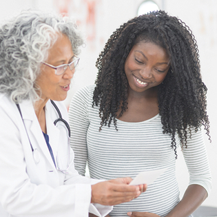 Image shows a female doctor speaking with a young Black female patient. 