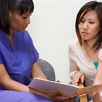 A Black nurse shares written information with an Asian patient. 