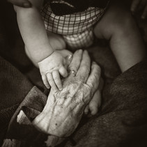 Black & white image shows a baby placing its hand over an elderly person's hand. 