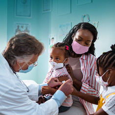 Image shows a Black family at a pediatrician's office, immunizing a Black baby girl