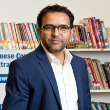 Photo of Sudarshan Pyakurel. He is a South Asian man with wavy hair and glasses. He is posing in front of a bookshelf. 