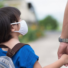 Image shows a young Asian girl holding her parent's hand as they walk to school
