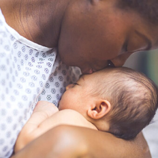 Image shows a Black mother lovingly kissing her baby's forehead