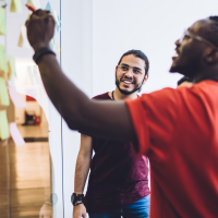 Man in a red shirt standing with a marker in front of a whiteboard.