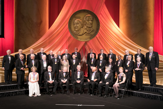 Men and women in black tie attire pose for a photo on a stage.