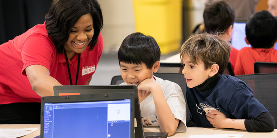 Smiling instructor works with two students on a project.