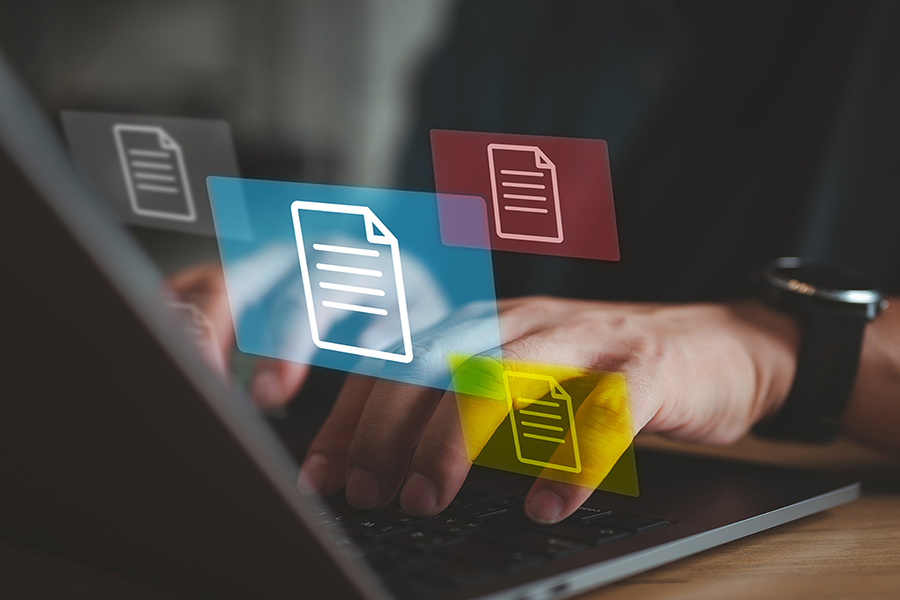 An image of a hands on a laptop keyboard with document icons hovering in the air