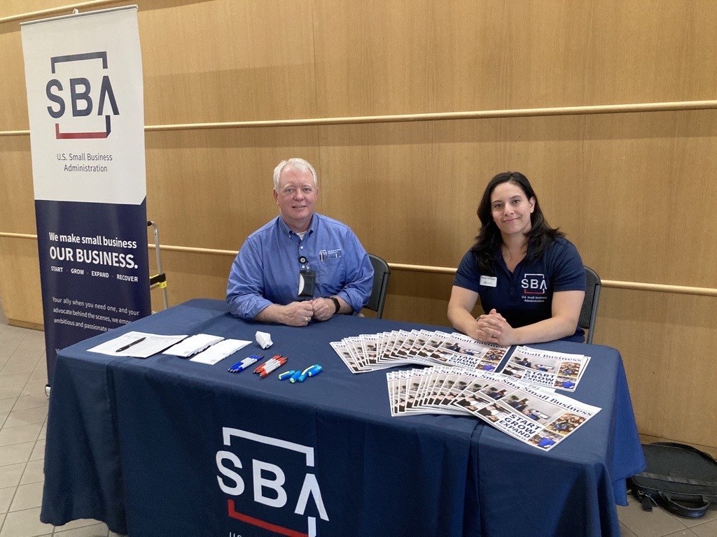 Two people sitting at a table with SBA logo on the front