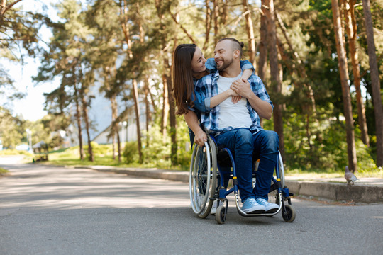Smiling woman embracing man in a wheelchair  