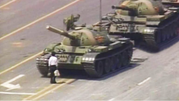 A man carrying shopping bags stands in front of tanks moving down the street.