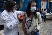 A woman in a white medical coat gives another woman a vaccine dose in her arm as they stand outside in Sao Paulo, Brazil. 