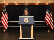 Undersecretary of State Patricia Nuland standing in front of  a podium next to two American flags.