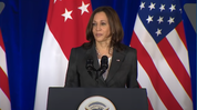 Vice President Harris speaks at a podium, with flags behind her.