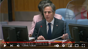 A photograph of Secretary Blinken speaking at the UN with a sign reading “United States” in front of him.
