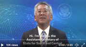 Assistant Secretary Don Lu in front of a blue screen with State Department seal and outline of Earth.
